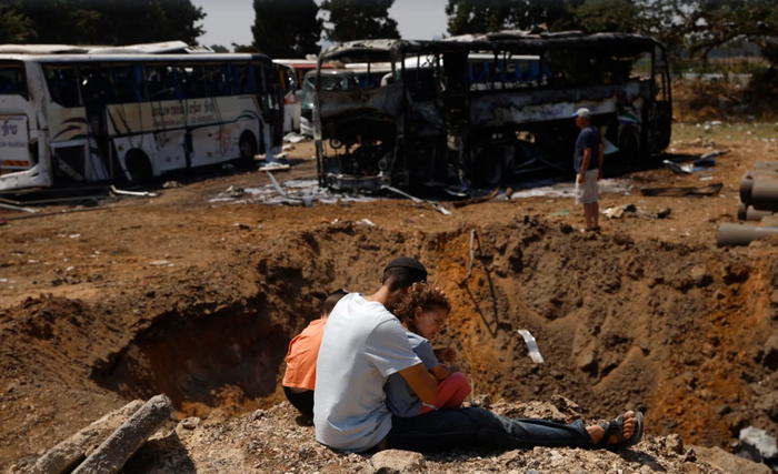 Люди смотрят на воронку в земле после ракетного удара 17 июня 2025 года в Герцлии, Израиль